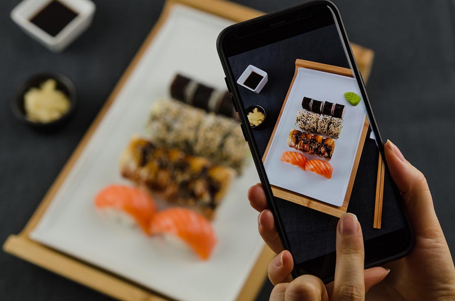 Pessoa tirando foto com um smartphone de um prato de comida japonesa