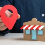 Mão segura pino de localização ao lado de uma loja miniatura para SEO local para pequenas empresas.