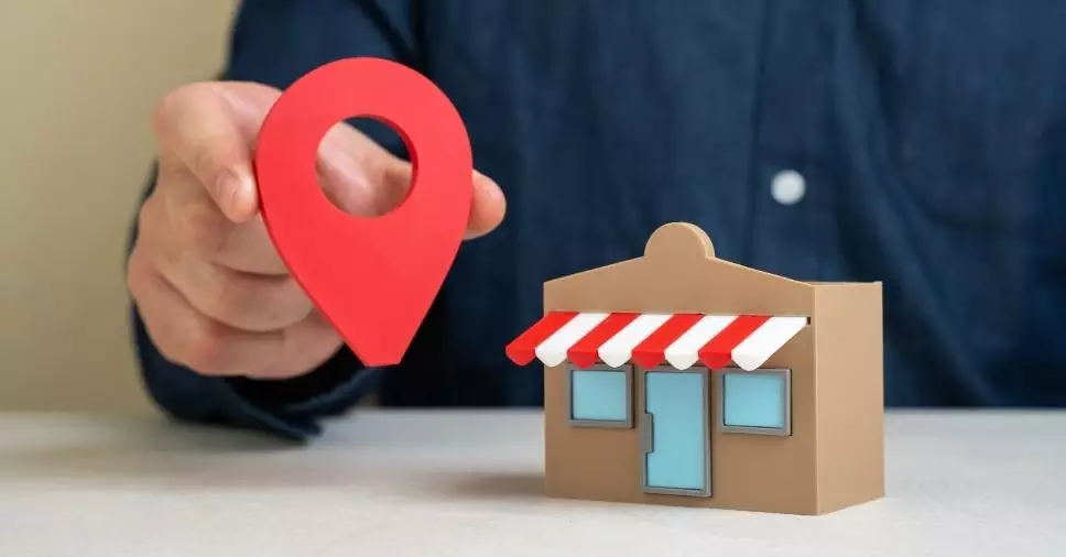 Mão segura pino de localização ao lado de uma loja miniatura para SEO local para pequenas empresas.