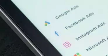 Entenda as diferenças entre Google Ads e Meta Ads com a Trii! Tela de smartphone exibe menus de ferramentas do Google Ads e Meta Ads.
